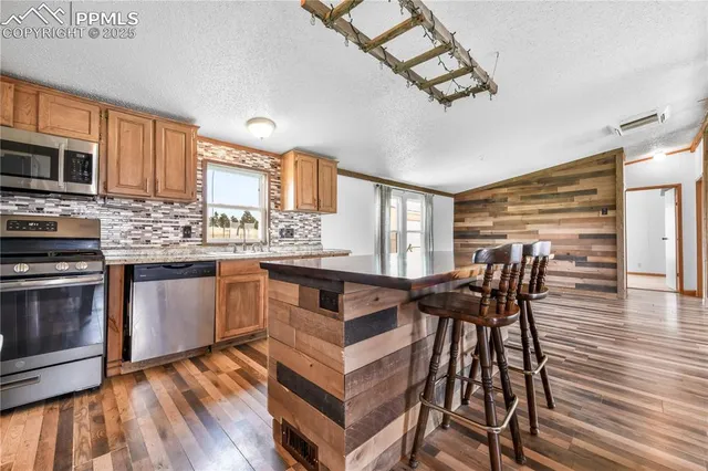 a kitchen with stainless steel appliances granite countertop a stove top oven a sink dishwasher a dining table and chairs with wooden floor