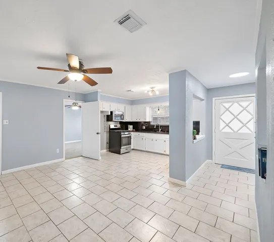 a view of an empty room and kitchen view with wooden floor