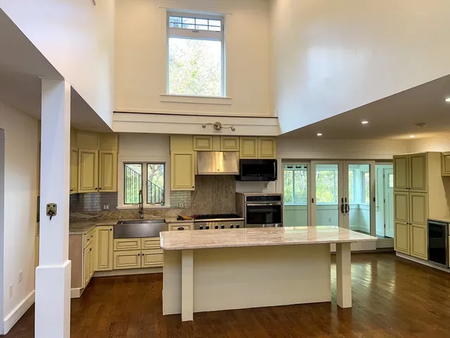 a living room with stainless steel appliances kitchen island granite countertop a stove a sink a refrigerator and white cabinets with wooden floor