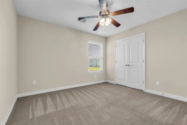 an empty room with chandelier fan and windows