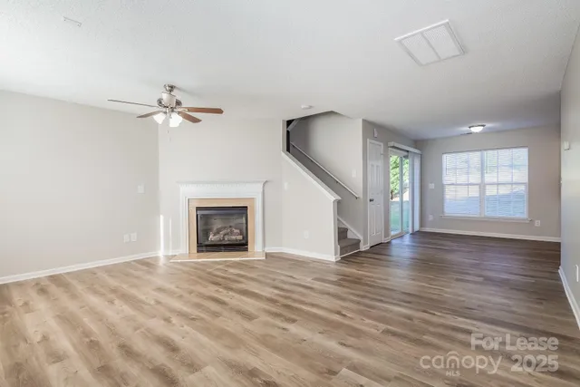 a view of an empty room with wooden floor fireplace and a window