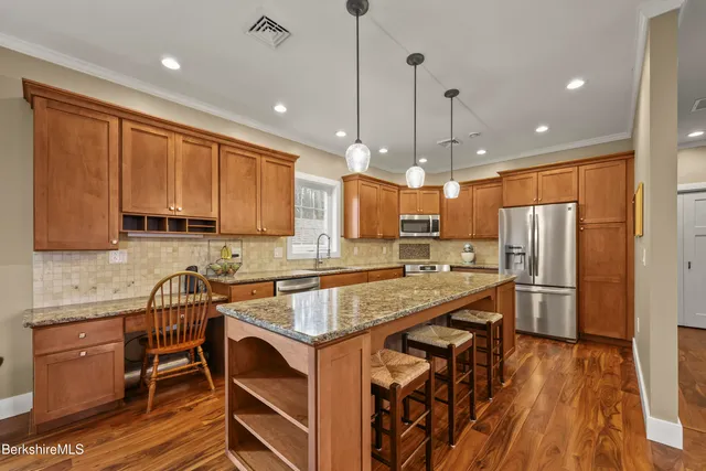 a kitchen with stainless steel appliances granite countertop a refrigerator a sink dishwasher a stove and white countertops with wooden floor