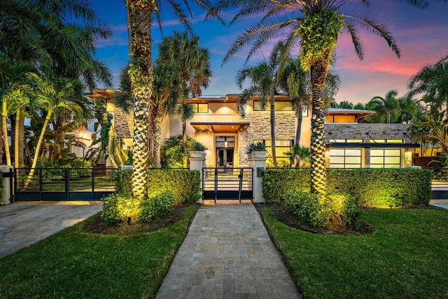 a view of a house next to a yard with plants and palm trees