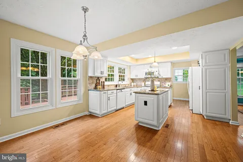 a kitchen with granite countertop a refrigerator a sink dishwasher a stove and white cabinets with wooden floor