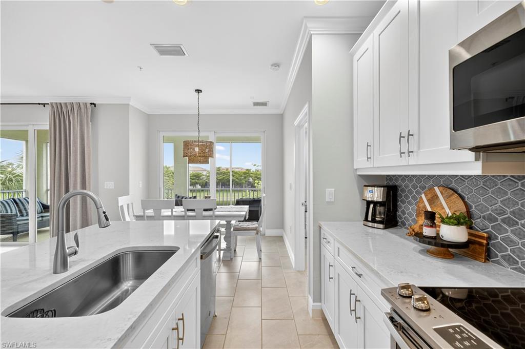 2319 Sawyers Hill Road, Unit 705 Naples, FL 34102 - Photo 11 of 29 Kitchen with white cabinetry, stainless steel appliances, light stone counters, crown molding, and backsplash