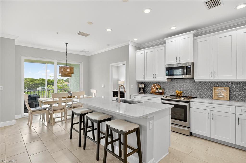 2319 Sawyers Hill Road, Unit 705 Naples, FL 34102 - Photo 8 of 29 Kitchen featuring ornamental molding, appliances with stainless steel finishes, light stone countertops, light tile patterned floors, and a breakfast bar area