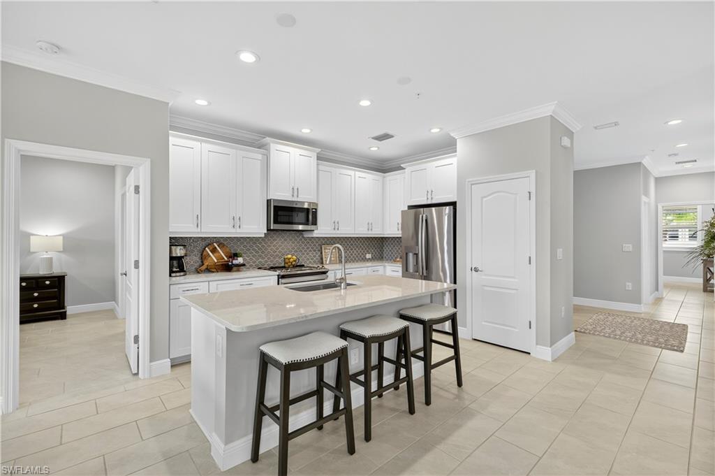 2319 Sawyers Hill Road, Unit 705 Naples, FL 34102 - Photo 9 of 29 Kitchen with light tile patterned floors, a breakfast bar area, crown molding, light stone countertops, and white cabinets
