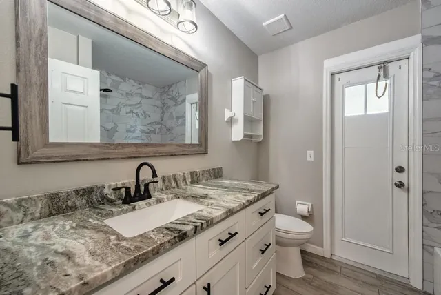 a bathroom with a granite countertop sink mirror vanity and toilet