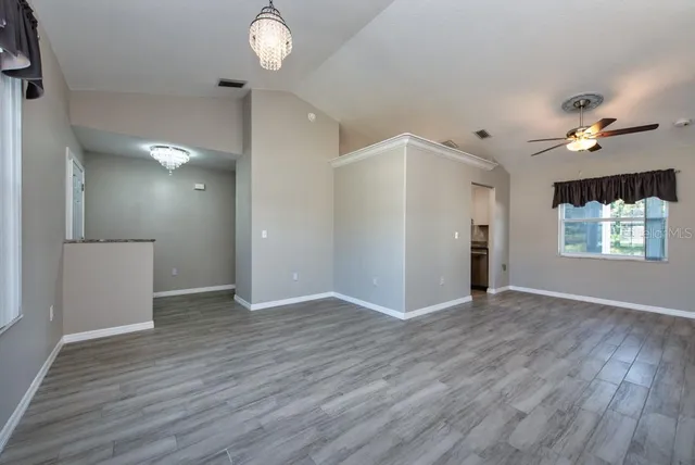 an empty room with wooden floor chandelier fan and windows