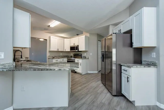 a kitchen with stainless steel appliances granite countertop a refrigerator stove a sink and white cabinets with wooden floor