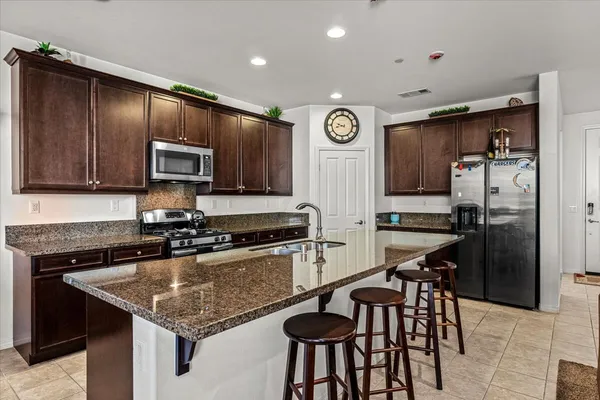 a kitchen with granite countertop a stove a sink dishwasher a dining table and chairs with wooden floor