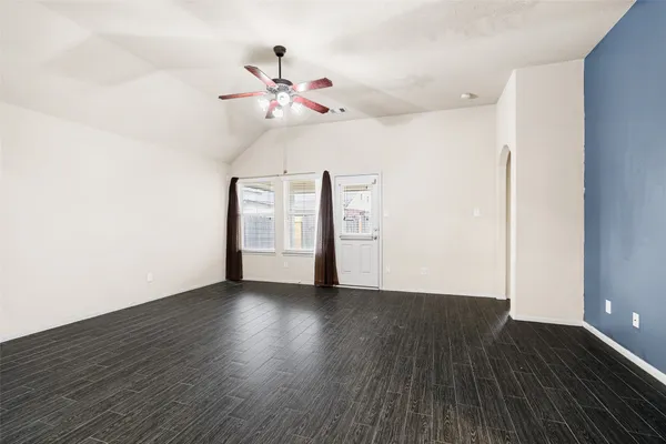 a view of an empty room with wooden floor and a ceiling fan