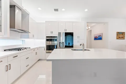 a large white kitchen with kitchen island a stove a sink a refrigerator and white cabinets