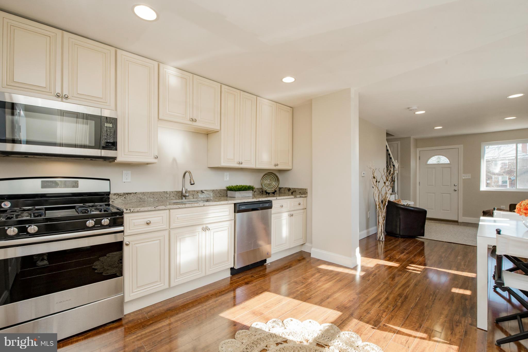 6922 Reisterstown Road Baltimore, MD 21215 - Photo 11 of 30 a kitchen with granite countertop a stove top oven a sink dishwasher and white cabinets with wooden floor