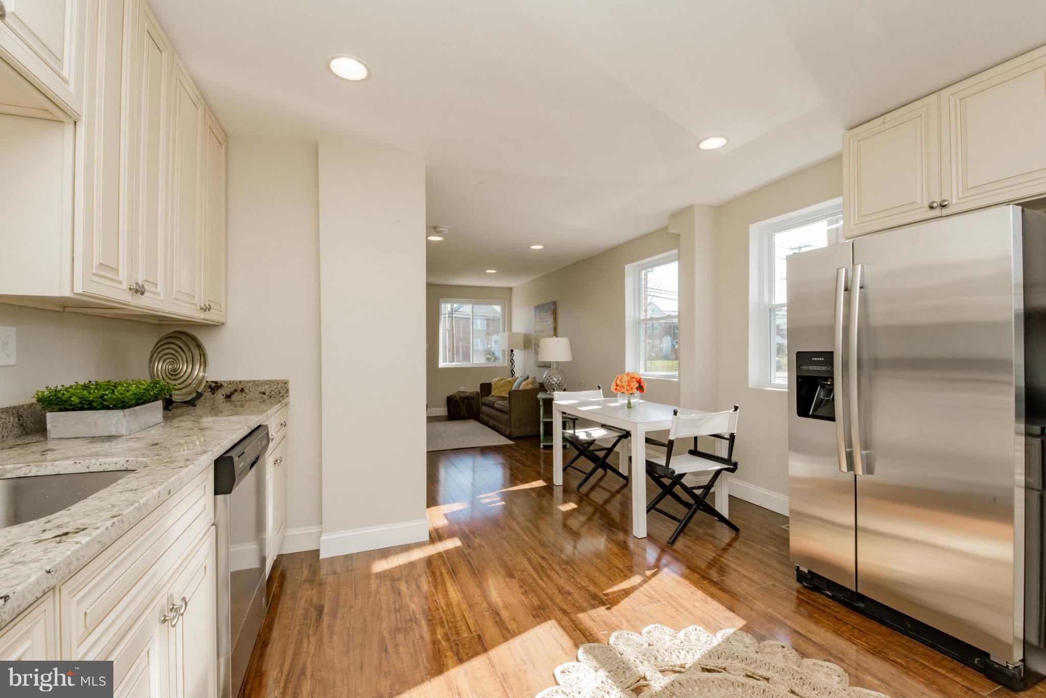 6922 Reisterstown Road Baltimore, MD 21215 - Photo 12 of 30 a kitchen with stainless steel appliances granite countertop a refrigerator a stove a dining table and chairs with wooden floor