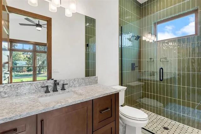 a bathroom with a granite countertop sink a toilet a mirror and shower