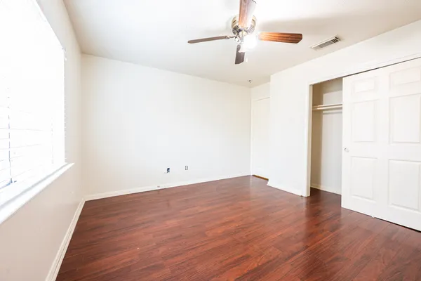 an empty room with wooden floor chandelier fan and windows