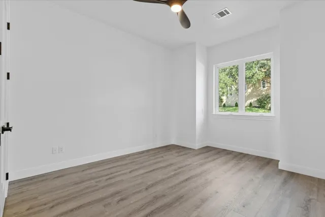 an empty room with wooden floor fan and windows