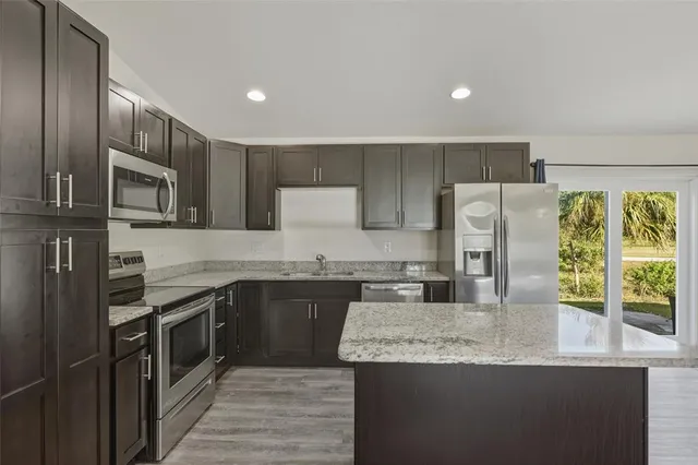 a kitchen with stainless steel appliances granite countertop a sink a stove a refrigerator a washer and dryer with wooden floor