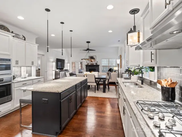 a large kitchen with stainless steel appliances kitchen island granite countertop a stove a sink a refrigerator and a dining table with wooden floor
