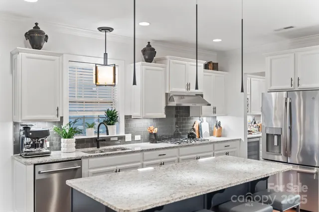 a kitchen with stainless steel appliances a sink a stove a refrigerator a center island and cabinets