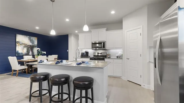 a kitchen with stainless steel appliances kitchen island granite countertop a stove top oven a sink dishwasher a dining table and chairs with wooden floor