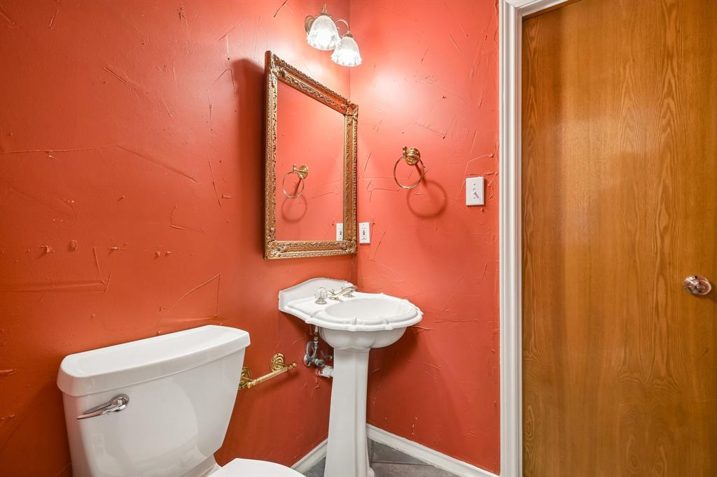 1380 Meandro Ria Lane Fairview, TX 75069 - Photo 23 of 39 Pedestal sink with a white basin and chrome fixtures, framed mirror with an ornate border, wall-mounted light fixture with two glass shades, and a wood-finish door