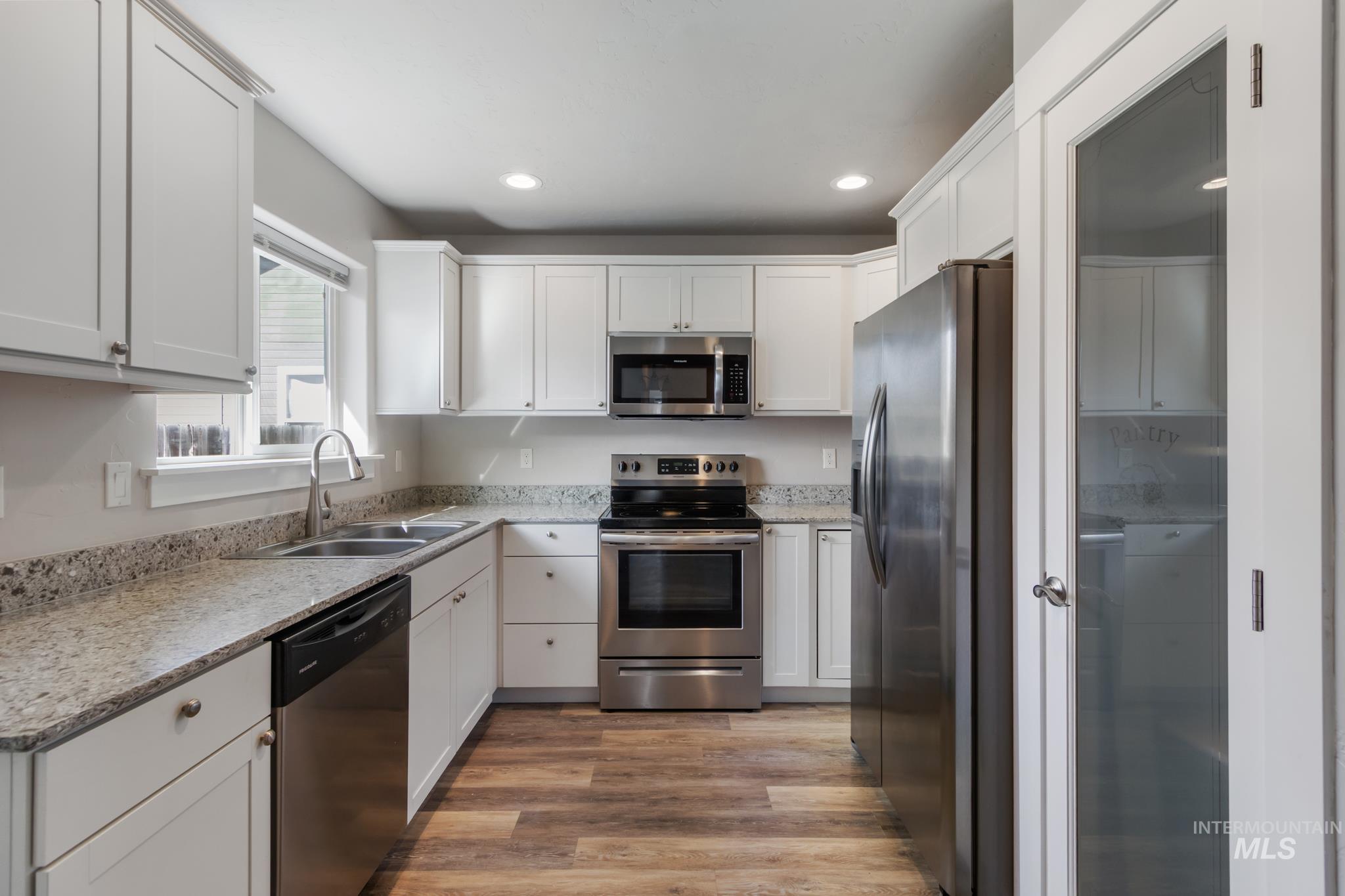 4822 Charme Street Caldwell, ID 83607 - Photo 6 of 22 Kitchen featuring stainless steel appliances, white cabinets, recessed lighting, light wood finished floors, and light stone counters