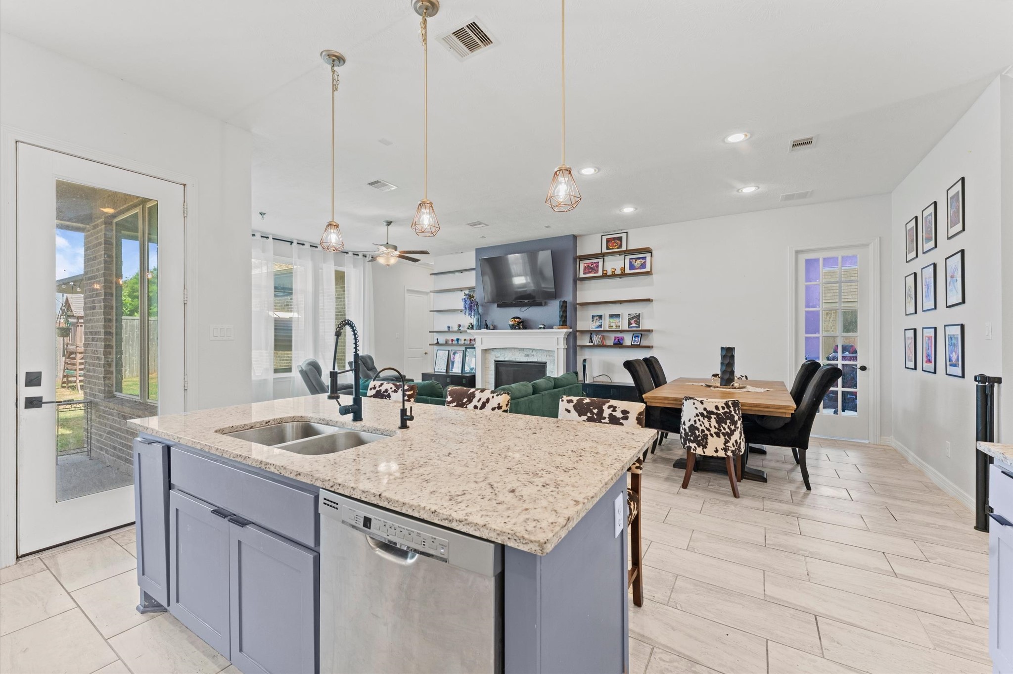 3510 Whitman Drive Rosharon, TX 77583 - Photo 6 of 25 This modern open-plan living space features a spacious kitchen island with granite countertops, pendant lighting, and stainless steel appliances. The cozy living area includes a fireplace and built-in shelves, while large windows and a glass door provide natural light and access to the backyard. The dining area is conveniently adjacent, offering a welcoming atmosphere for entertaining.