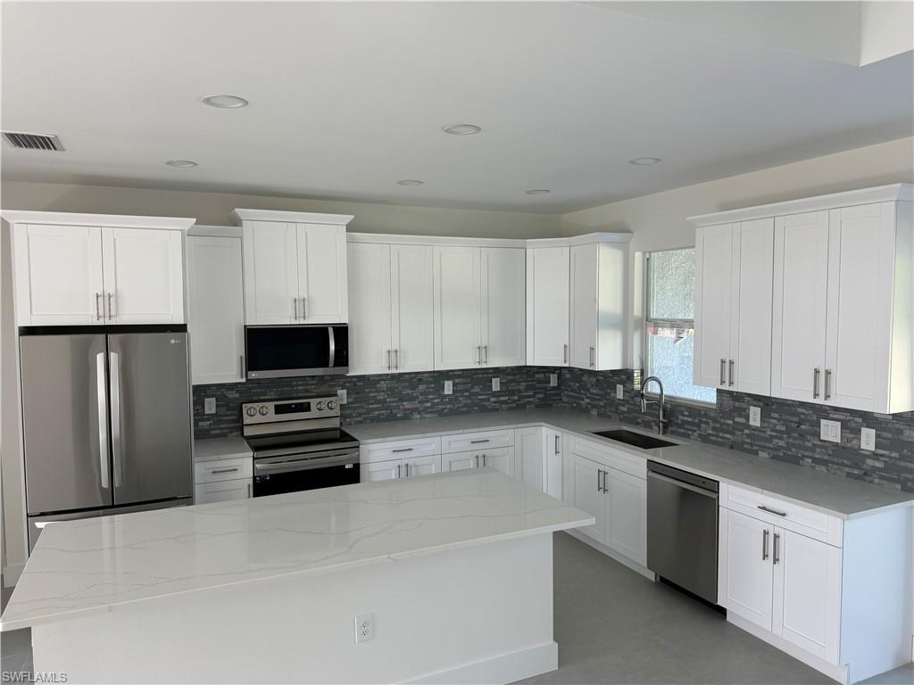 829 Albert Avenue Lehigh Acres, FL 33971 - Photo 10 of 27 a kitchen with stainless steel appliances a stove a sink a refrigerator a window and white cabinets