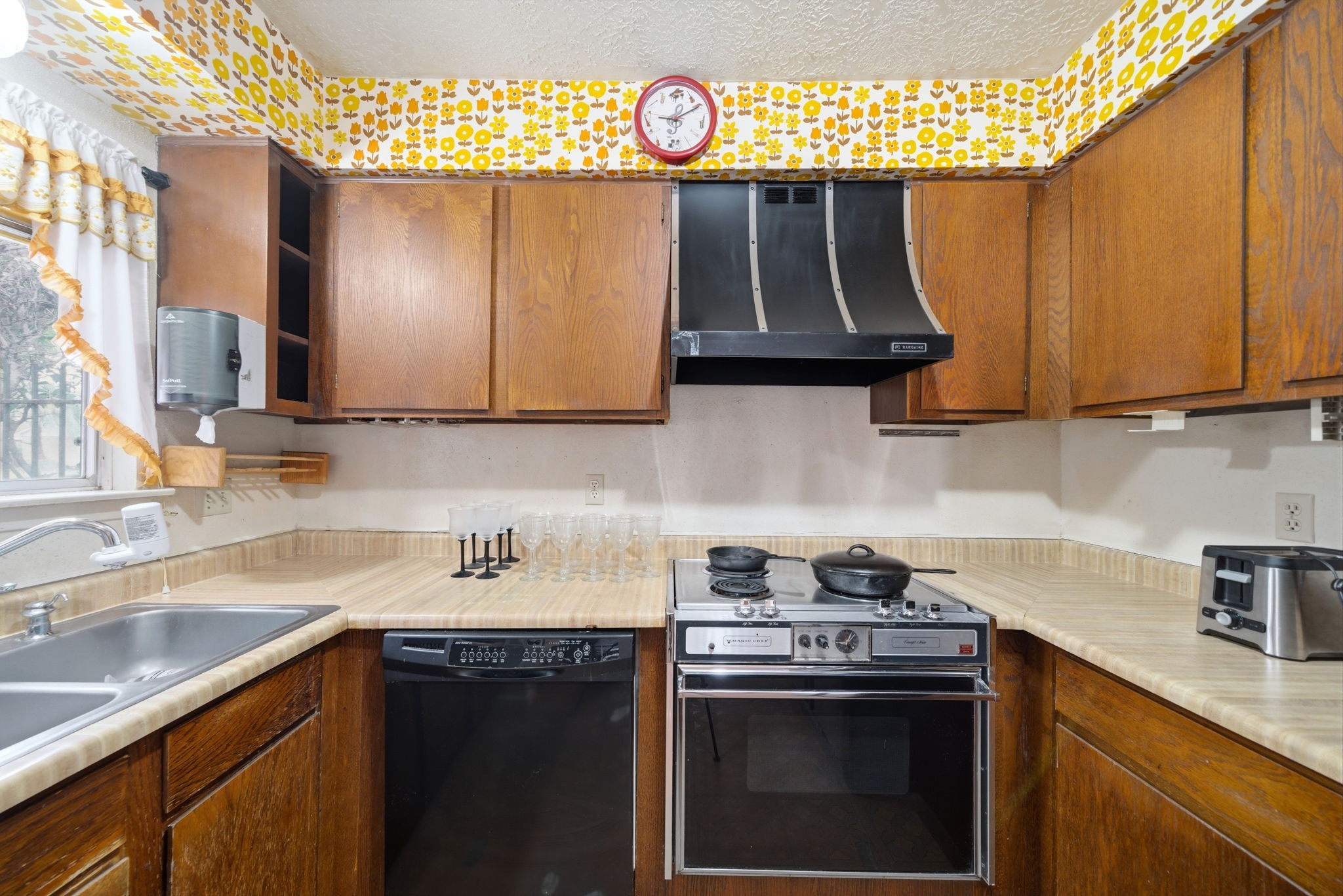 5822 Skewen Street Humble, TX 77346 - Photo 16 of 29 This cozy kitchen features warm wooden cabinetry and retro appliances, accented by a colorful, floral wallpaper border. The double sink under the window brings in natural light, and ample countertop space provides functionality for cooking and entertaining.