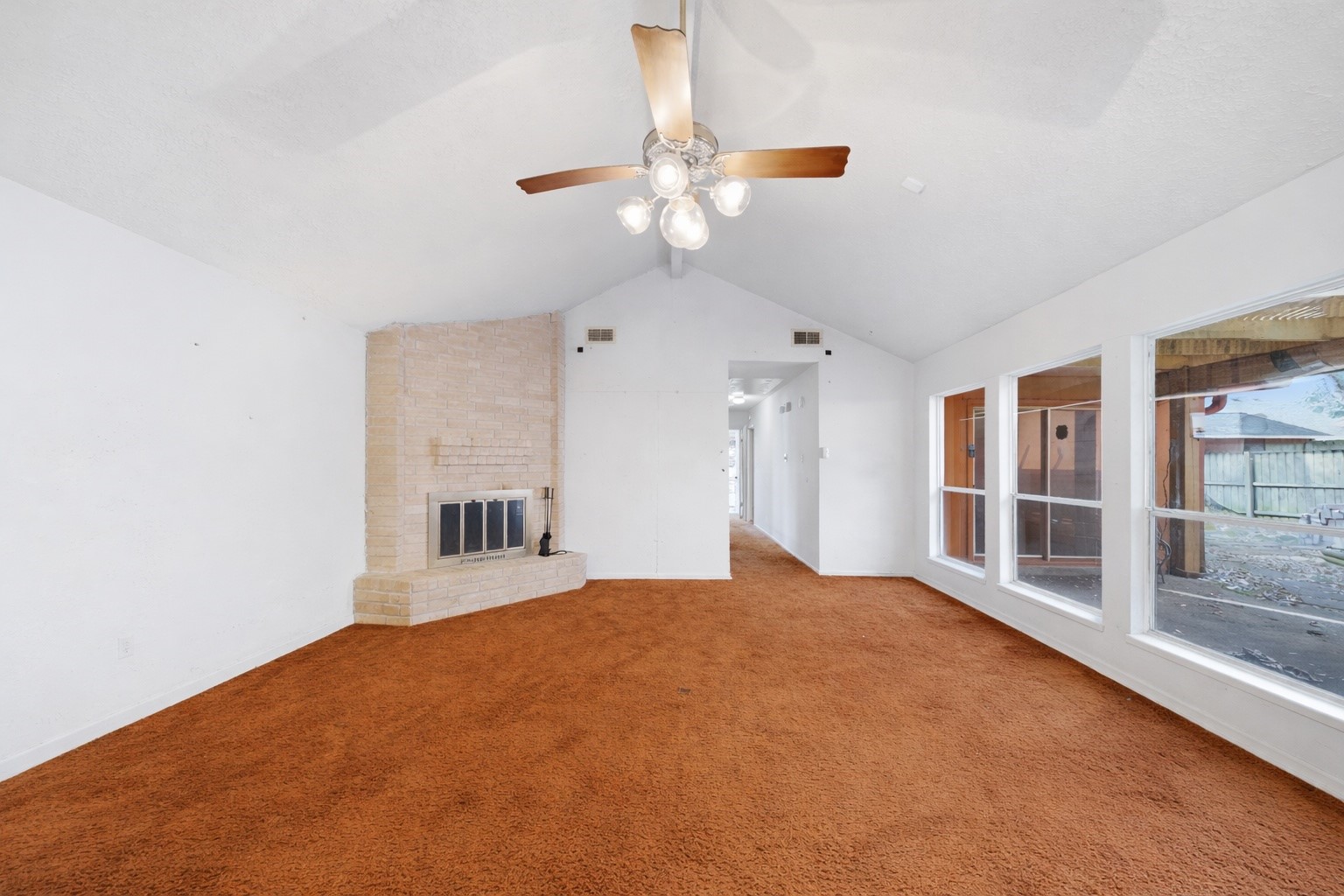 5822 Skewen Street Humble, TX 77346 - Photo 6 of 29 The spacious living room features a cozy brick fireplace, large windows for natural light, and a ceiling fan. The room has a warm, carpeted floor and a high, sloped ceiling, creating an inviting atmosphere.