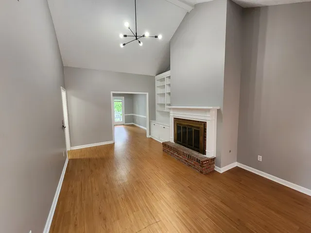 an empty room with wooden floor fireplace and chandelier