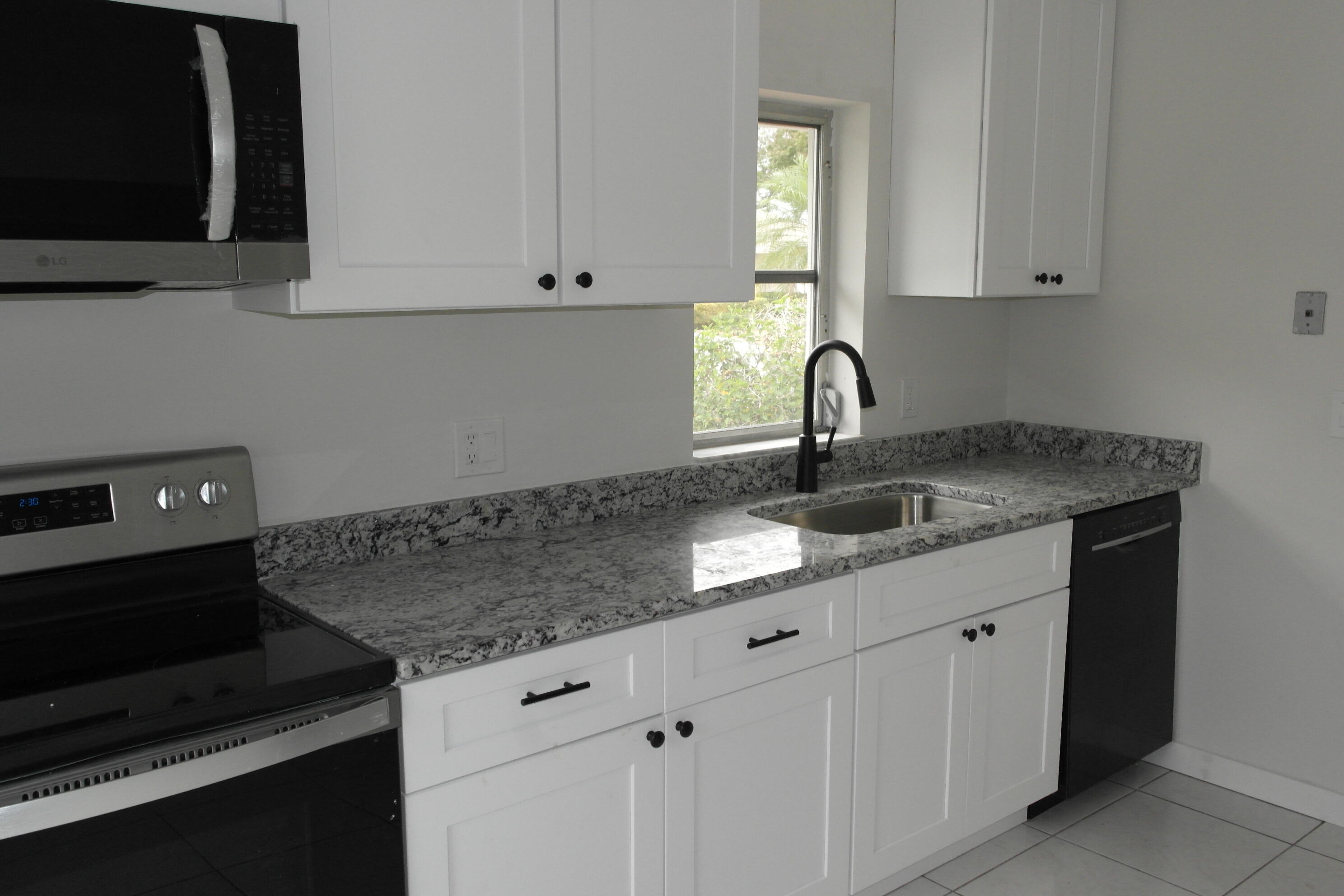 18890 Candlewick Drive, Unit B Boca Raton, FL 33496 - Photo 4 of 16 a kitchen with granite countertop a sink dishwasher a stove and a microwave oven with white cabinets
