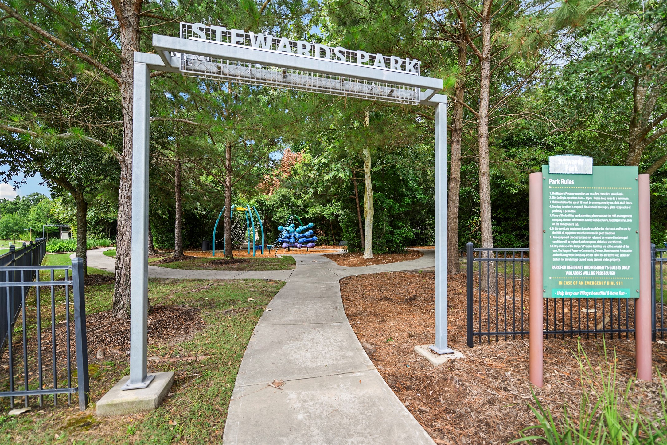 10603 Whitejacket Conroe, TX 77385 - Photo 41 of 42 This photo shows the entrance to a park with a sign reading "Stewards Park." The park features a paved path, surrounded by trees, leading to a playground area with climbing structures. It's a serene, green space ideal for families and outdoor activities.