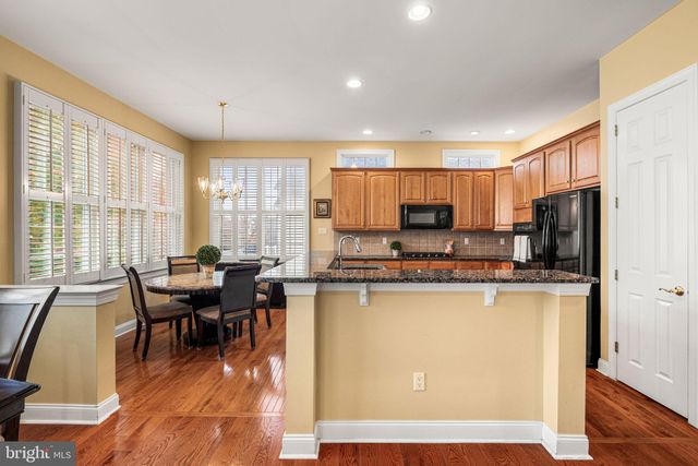 a living room with stainless steel appliances a dining table wooden floor windows and a kitchen view