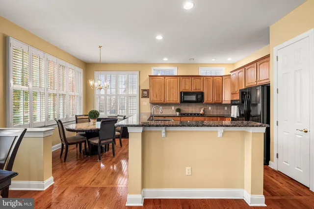a living room with stainless steel appliances a dining table wooden floor windows and a kitchen view
