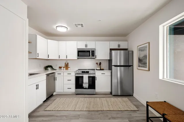 a kitchen with stainless steel appliances granite countertop a stove top oven a refrigerator a sink and dishwasher with white cabinets