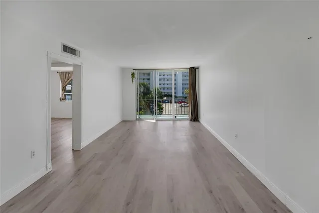 a view of an empty room with wooden floor and a window