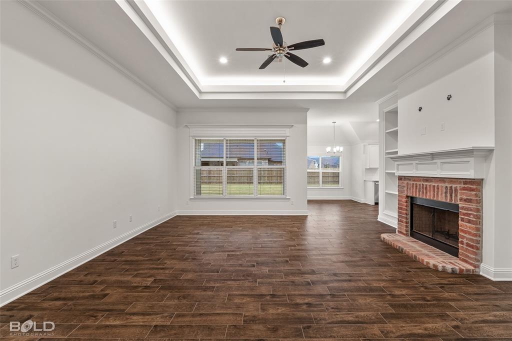 304 Prien Lk Loop Bossier City, LA 71111 - Photo 10 of 39 Spacious living area featuring wood-finish flooring, a tiered tray ceiling with recessed lighting and a ceiling fan, a brick fireplace with a white mantel, and built-in shelving