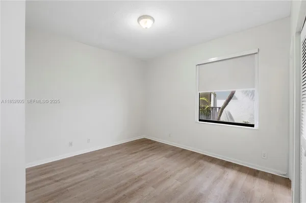 a view of an empty room with wooden floor and a kitchen
