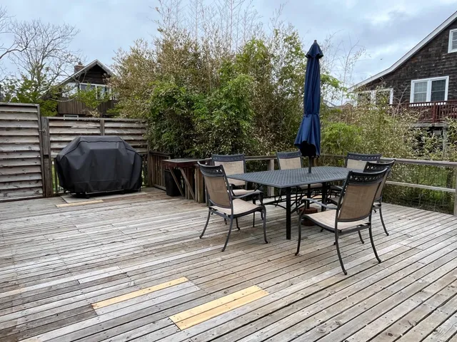 a view of a roof deck with table and chairs a barbeque with wooden floor and fence