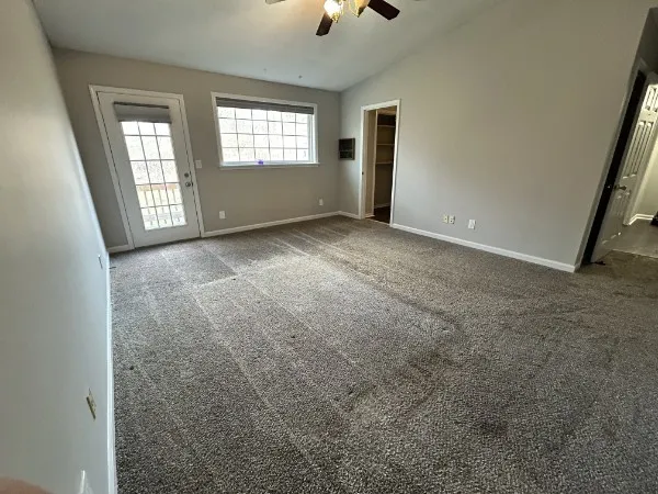 an empty room with ceiling fan and windows