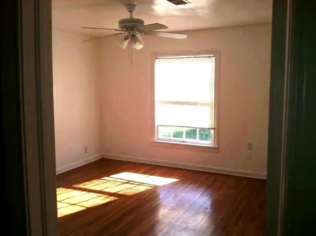 an empty room with wooden floor fan and windows
