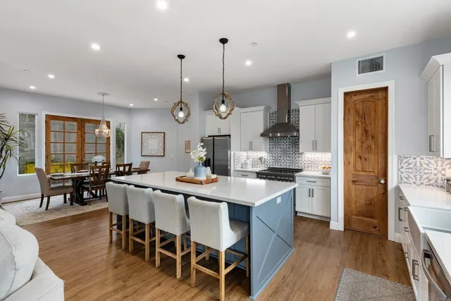 a large kitchen with stainless steel appliances kitchen island granite countertop a stove a sink a refrigerator and a dining table with wooden floor