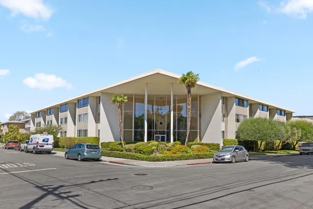 a view of a brick house with potted plants and a small yard