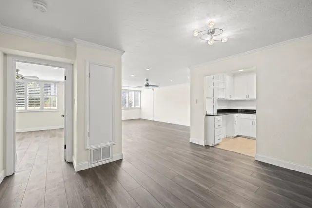 a view of empty room with wooden floor and kitchen