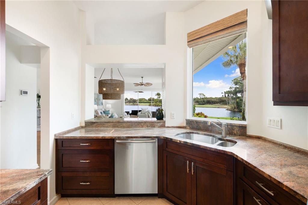2153 Paget Circle Naples, FL 34112 - Photo 29 of 49 Kitchen with stainless steel dishwasher, dark brown cabinets, light stone counters, light tile patterned floors, and a water view