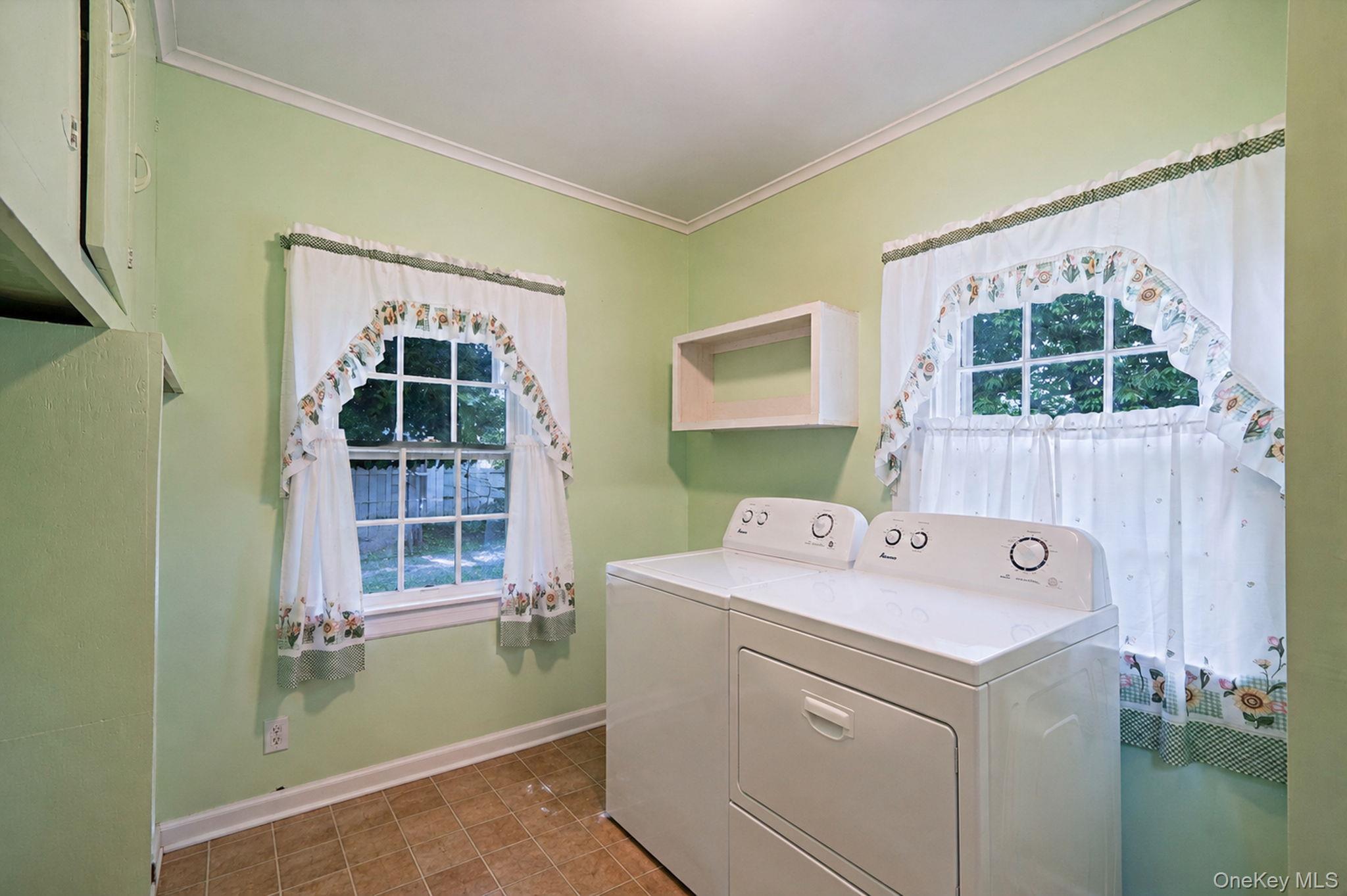 1055 Oregon Road Mattituck, NY 11952 - Photo 20 of 33 Laundry room featuring dual windows, crown molding, a built-in wall cabinet, and durable tile-finish flooring