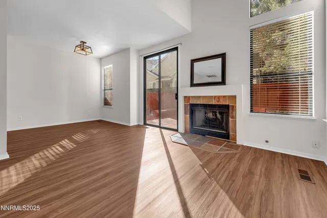 a view of an empty room with wooden floor fireplace and a window
